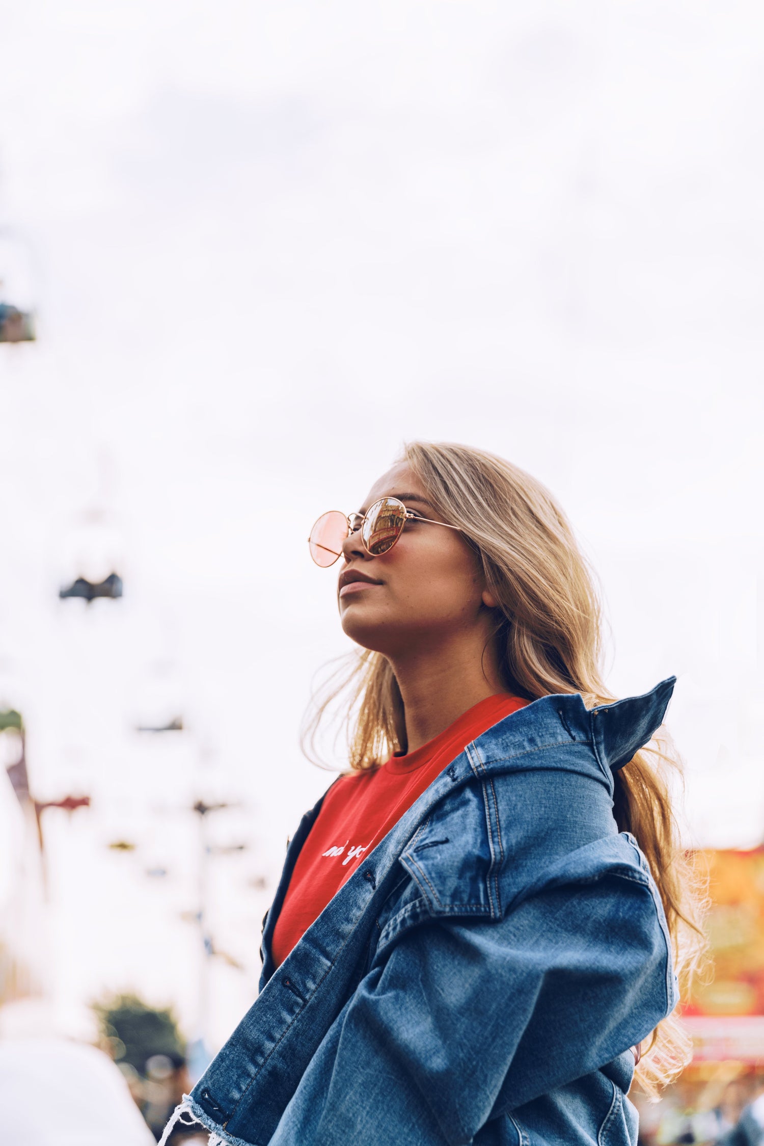 A young lady wearing a denim jacket, red top and sunglasses.